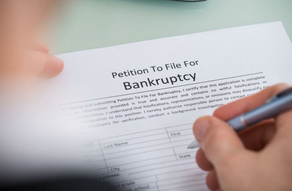 A close-up photo of a person's hand holding a pen and filling out a bankruptcy form