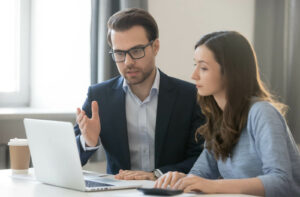 A professional-looking young man showing a young woman something on a laptop.