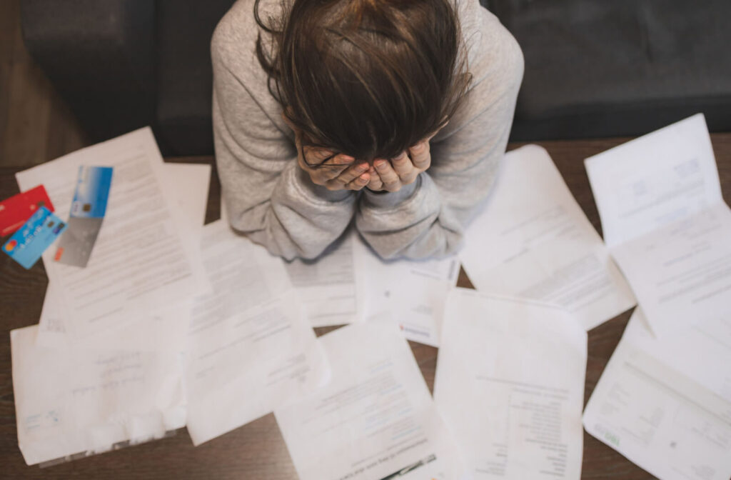 A woman is sitting on a chair with credit cards and plenty of billing statements and demand letters from the bank about loans and unpaid bills on the table  is getting stressed and frustrated.