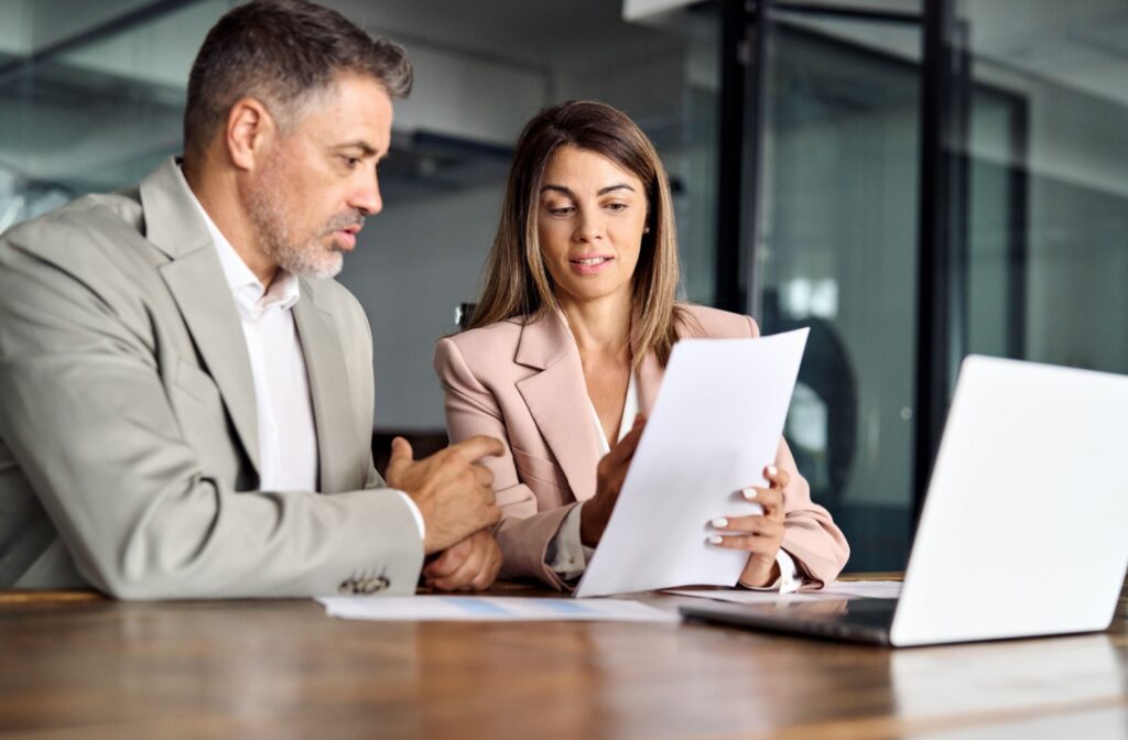 A man in a suit meeting with his lawyer as she shows him a debt document while they sit at a table.