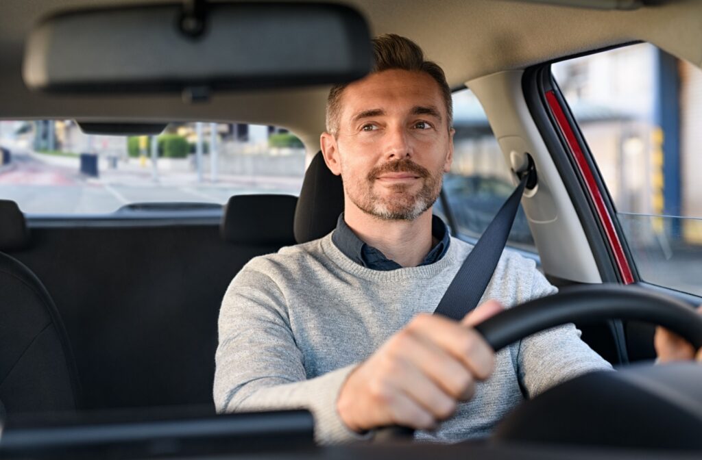 A man in a sweater and collared shirt looking in his rearview mirror as he drives.