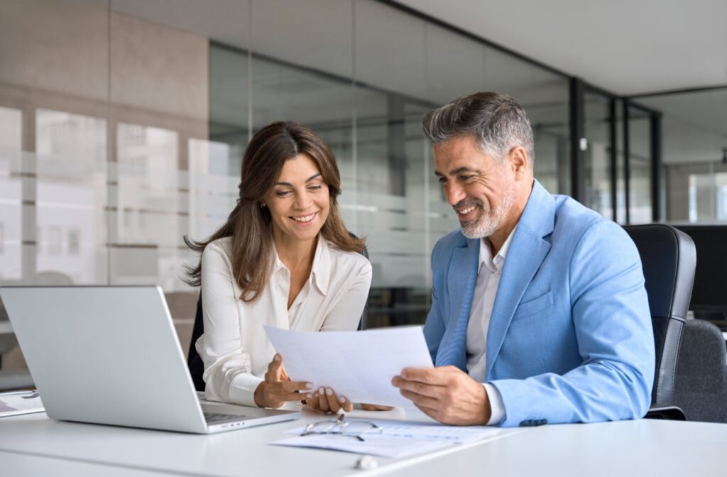 A financial advisor and their client sit at a table in front of a laptop, looking over a printout.