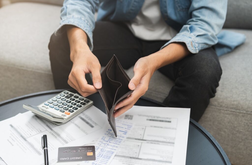 someone sitting at a table holding open an empty wallet with a calculator, credit card, and calculator in front of them.