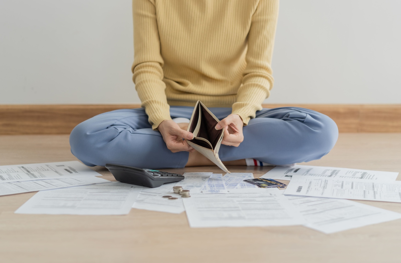 A person sitting on the floor surrounded by documents opens their empty wallet.