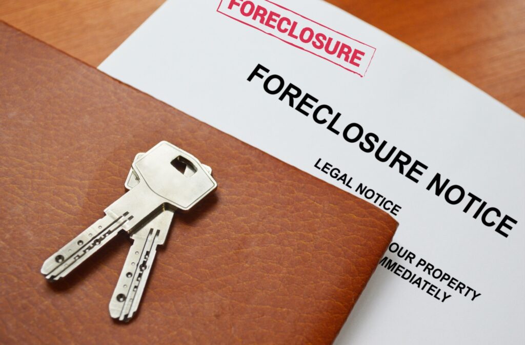 A piece of paper labelled "foreclosure notice" laying on a desk with a pair of keys on top.