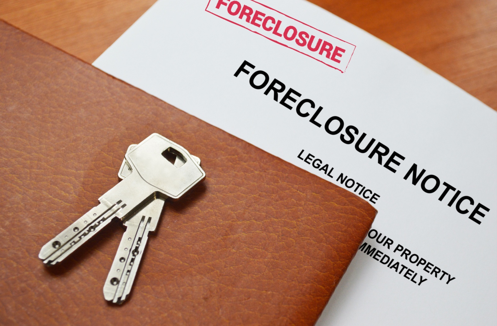 A piece of paper labelled "foreclosure notice" laying on a desk with a pair of keys on top.